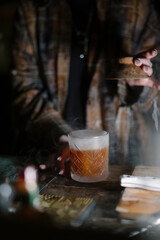 Female bartender standing by the bar counter, making a cocktail, smoking the glass, close up vertical image
