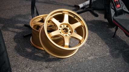 Pair of gold six-spoke alloy wheels on asphalt. Two aftermarket bronze forged rims resting on an...
