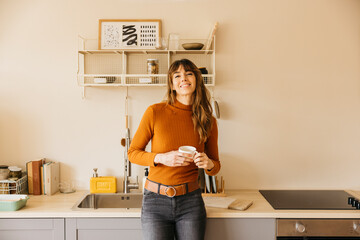 Woman smiling holding coffee mug in modern kitchen