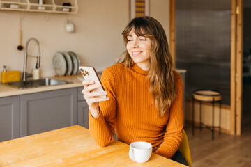 Woman smiling using smartphone having breakfast at home