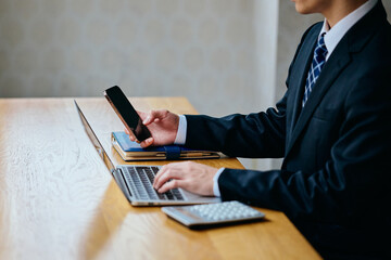Businessman Using Smartphone While Working on Laptop at Office Desk