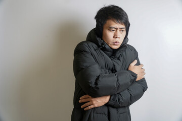A man in a thick black puffer jacket is shivering from the cold, hugging himself to stay warm © yashis007