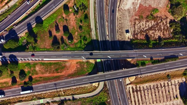 Cars move along a busy highway featuring multiple lanes and intersections. Green areas and brown land are visible on both sides. The scene captures a normal day of travel.