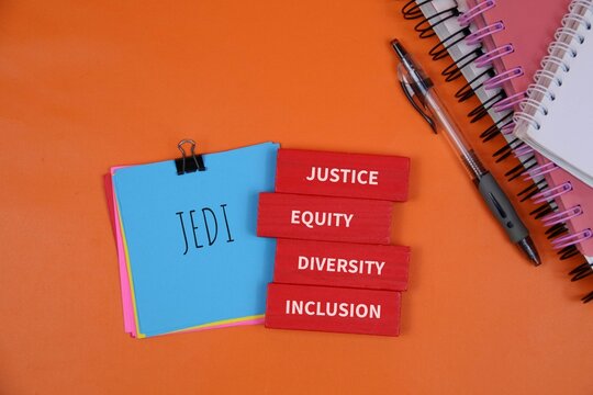 blue Jedi notebook and red blocks reading Justice, Equity, Diversity, and Inclusion, symbolizing diversity and inclusive teamwork in education and work environments. isolated on orange background.