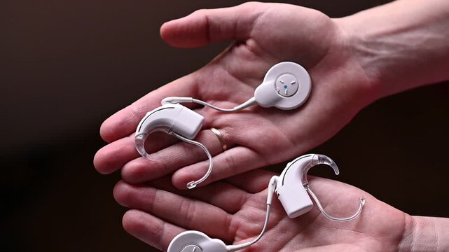 Modern cochlear implant devices resting in open hands. Advanced medical technology for people with severe hearing loss. Audiology, hearing rehabilitation and healthcare concept.