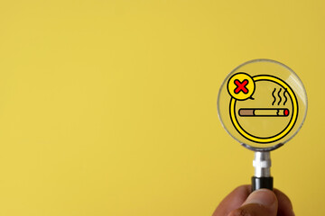 World No Tobacco Day and lung cancer awareness. Hand holding magnifying glass with stop smoking icon. Symbol of quitting cigarette, forbidden sign, and healthy breath on yellow background.,copyspace.