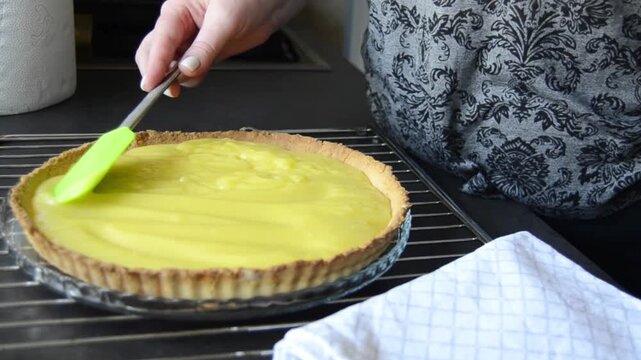 Hands smoothing out a lemon curd on a baked short crust pastry crust.