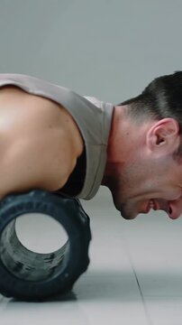 Vertical video: Shifting weight man in gray top pressing foam roller on tile floor releasing pain