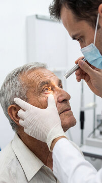 Doctor performing detailed eye examination on senior man using penlight to evaluate pupil reaction in clinical ophthalmology checkup.