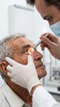 Doctor performing detailed eye examination on senior man using penlight to evaluate pupil reaction in clinical ophthalmology checkup.