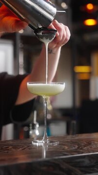 the bartender's hands pour a beautiful cocktail from a shaker in a bar or restaurant vertical video slow motion close-up