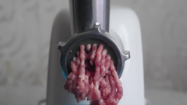 Close-up of an electric meat grinder processing fresh raw meat into minced meat. The process of making homemade forcemeat for cutlets or meatballs in a blue bowl