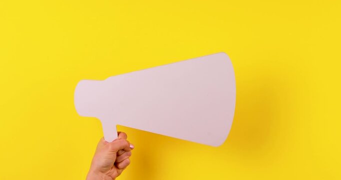 Close-up of hands holding a megaphone symbol twitching on a bright yellow background. Concept of loud advertising, promotion, announcements, marketing communication, and attention grabbing. Isolated, 