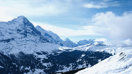 Snow-covered peaks of the Swiss Alps under a clear blue sky with scattered clouds, showcasing the majestic mountain range and pristine winter landscape