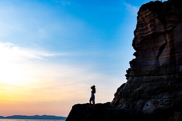 Beautiful young woman silhouette standing on stone at sunset or sunrise sky over sea
