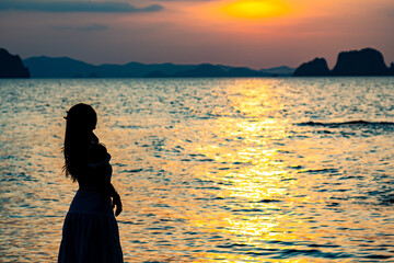 Beautiful young woman silhouette standing on stone at sunset or sunrise sky over sea