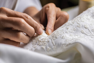 Close-up of hands meticulously embroidering white fabric, showcasing the elegant designs and textures that elevate the artistry of textile craftsmanship.