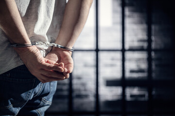 Arrested criminal wearing handcuffs with handcuffed hands behind back in prison