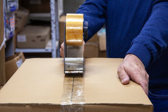 Man Sealing Cardboard Box with an Adhesive Tape