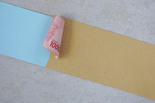 Finance concept using Indonesian Rupiah banknotes sticking out from brown envelope with blank paper note for text design on grey surface