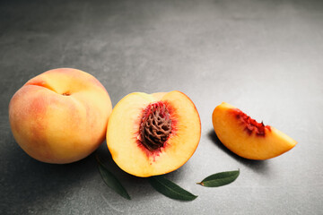 Fresh whole and sliced peaches with green leaves on a dark grey background