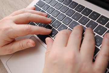 Close-up of female hands typing on a modern laptop keyboard in a home office.