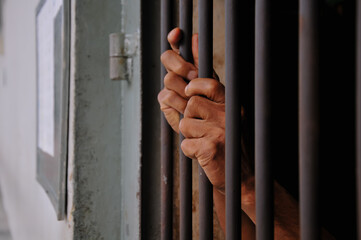 Obraz premium prisoner's hands behind bars at black background