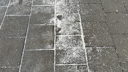 Fototapeta premium Excess road salt on urban sidewalk in winter. Close-up of deicing material used for snow and ice control in city environment.