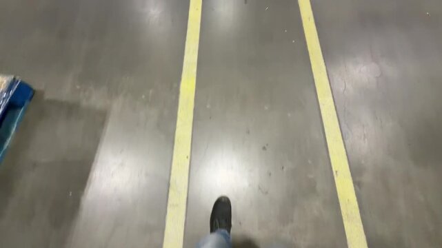 Point of view walking through an industrial warehouse following yellow safety lines over a yellow pedestrian icon