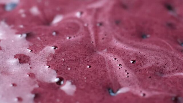 Fresh blueberries with water droplets are ready for blending. Thick, vibrant blueberry smoothie is poured over the berries.