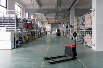 A warehouse aisle with an electric pallet truck parked and shelves fully stocked with goods © zhu difeng