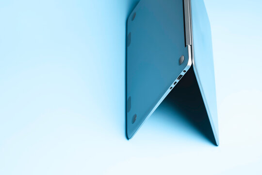 Open laptop stands upside down on surface against blue background.