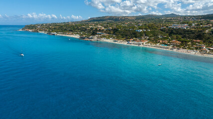 Fototapeta premium Aerial view of a vibrant blue coastline. The deep azure sea meets a white sandy shore lined with lush green hills, coastal villages. It's Tono Beach, located in Calabria in the coast of Gods, Italy.