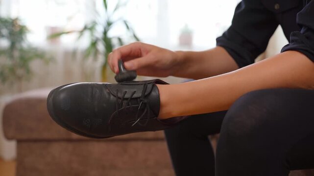 Close-up of a person sitting indoors while carefully cleaning and shining black leather footwear with a polish applicator sponge, meticulously preparing the shoes for a formal event