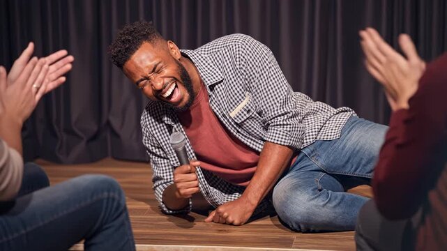 joyful stand up comedian lying on stage while performing a comedy routine, surrounded by an applauding audience, capturing humor, entertainment, and live performance atmosphere