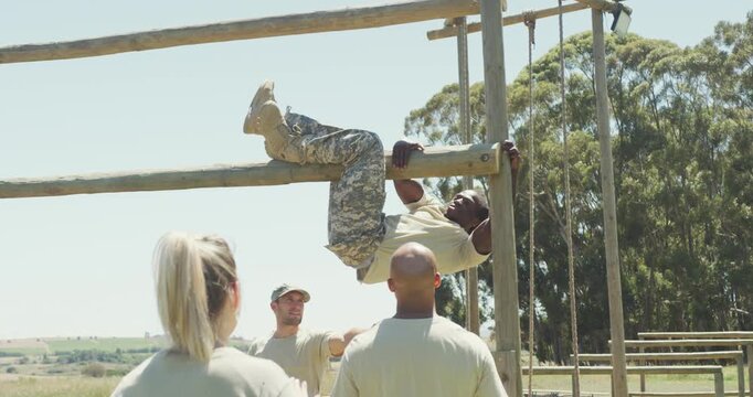 Diverse group watching fit african american male soldier with deadlocks climbing on obstacle course