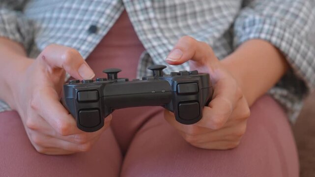 Unrecognizable woman holding a joystick and playing video games on a console at home, pressing the buttons on the controller and having fun during her leisure time on the couch