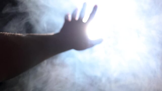 Close-up video with soft focus of a male hand reaching toward a powerful, voluminous projector light cutting through haze. Concept of striving for truth and enlightenment.