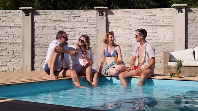 Group of adult friends sitting and relaxing next to outdoor pool.