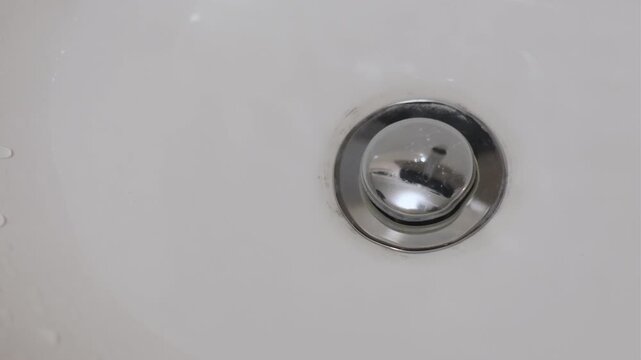 Finger pressing a pop-up sink drain stopper creating a mechanical click and gurgling water sound