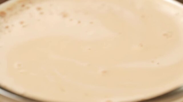 Macro shot of light brown milk foam or crema surface texture on a hot latte or cappuccino, providing an abstract, creamy background.