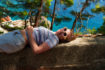 Cheerful girl in sunglasses lying near the sea, smiling portrait during summer holiday in...