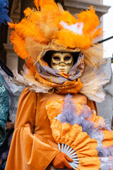 Close-up portrait of a Venetian carnival mask in an ornate orange costume with feathers during Carnival in Venice, Italy