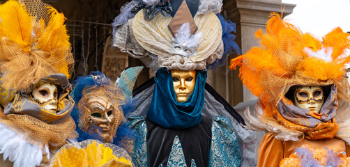 Three performers in elaborate Venetian carnival costumes pose under historic arcade in Venice