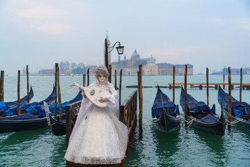 Elegant performer in white Venetian carnival costume playing a lute near gondolas on the lagoon in Venice, Italy