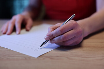 A focused hand with a silver pen marks off items on a checklist placed on a smooth wooden surface. The warm light creates a productive atmosphere for planning.
