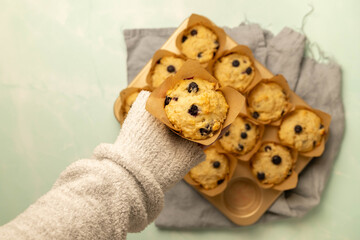 Close-up of a fresh baked blueberry muffin held above more muffins with blue marbled background