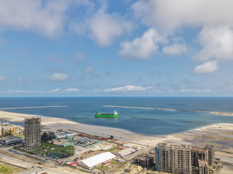 Aerial view of a vibrant green cargo ship sailing through the tranquil blue waters near the shore, contrasting with the developing cityscape, Lagos, Lagos, Nigeria.