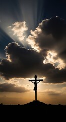 Jesus Christ on the cross silhouette against a dramatic sunset sky with sun rays shining through clouds. Religious symbol of faith for Easter and Good Friday.