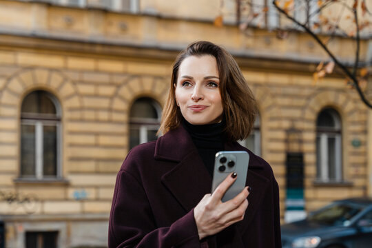 Confident woman holding smartphone on city street in autumn